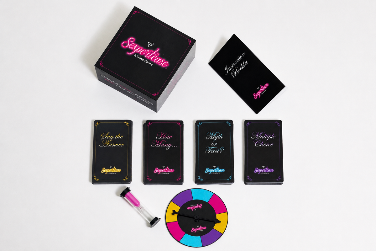 Sexpertease game set arranged on a white background, including a black box, instruction booklet, the four category tuck boxes, a spinner, and a small pink-and-black timer.