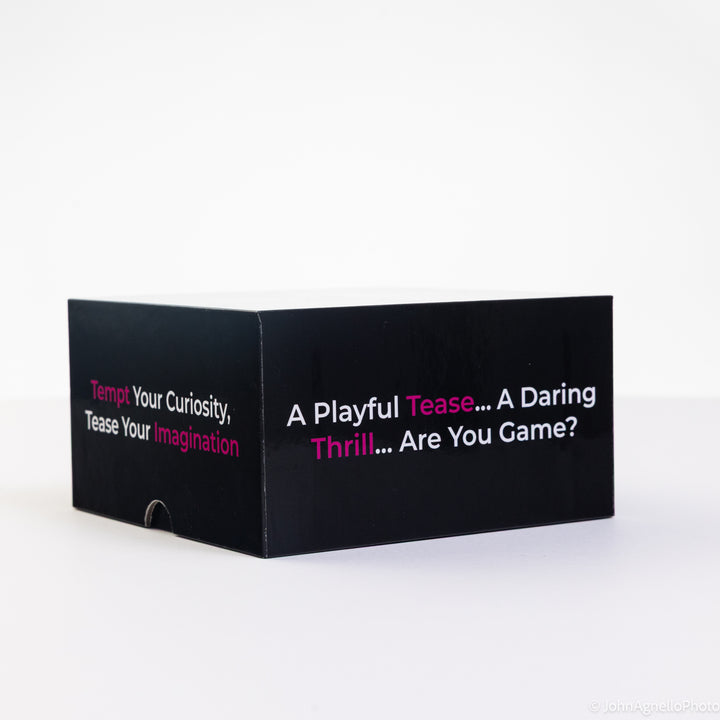 A black rectangular product box with white and pink text, photographed on a clean white studio background. The visible text reads, &