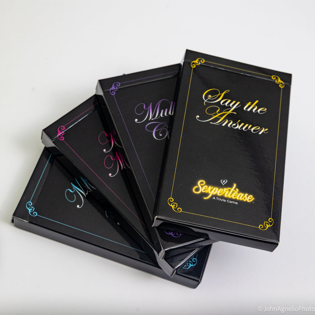 Four black playing card decks fanned out on a white surface, each with a different colored border accent (blue, pink, purple, gold) and the title &