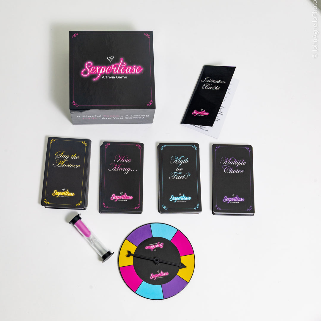 Serpertease A Trivia Game set arranged on a white background, including a black box with pink logo, instruction booklet, four tuck boxes with colorful text, a small pink-and-clear timer, and a colorful spinner wheel.